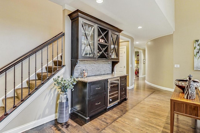 bar featuring light hardwood / wood-style flooring, light stone counters, dark brown cabinetry, and wine cooler