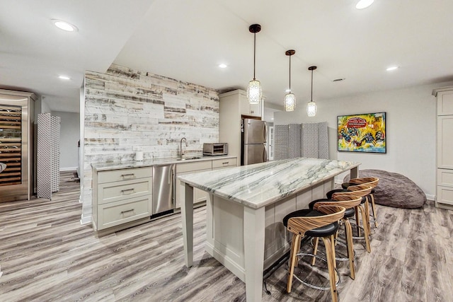 kitchen featuring stainless steel appliances, wooden walls, a center island, decorative light fixtures, and light stone countertops