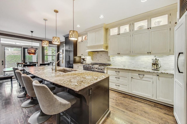 kitchen with light stone counters, premium appliances, decorative light fixtures, a center island with sink, and sink