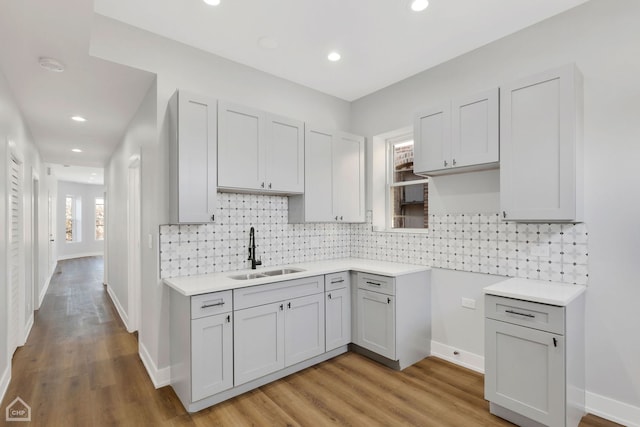 kitchen with gray cabinetry, sink, backsplash, and light hardwood / wood-style flooring