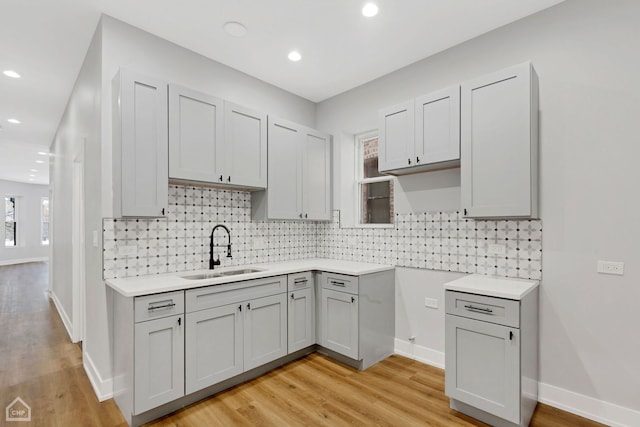 kitchen featuring light wood-type flooring, backsplash, sink, and gray cabinetry