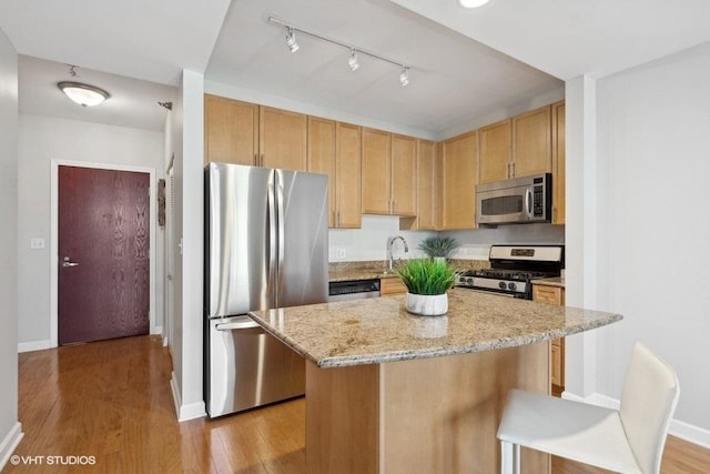 kitchen with a kitchen bar, appliances with stainless steel finishes, light stone countertops, a center island, and light hardwood / wood-style floors