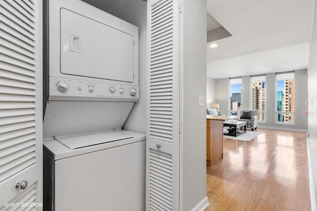 clothes washing area featuring stacked washing maching and dryer and light hardwood / wood-style flooring