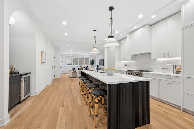 kitchen featuring white cabinets, pendant lighting, beverage cooler, premium range hood, and a kitchen island with sink