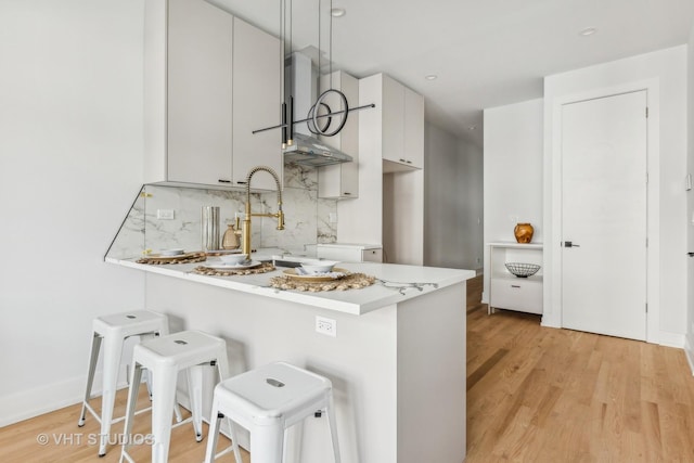 kitchen with a kitchen breakfast bar, kitchen peninsula, white cabinets, and wall chimney range hood