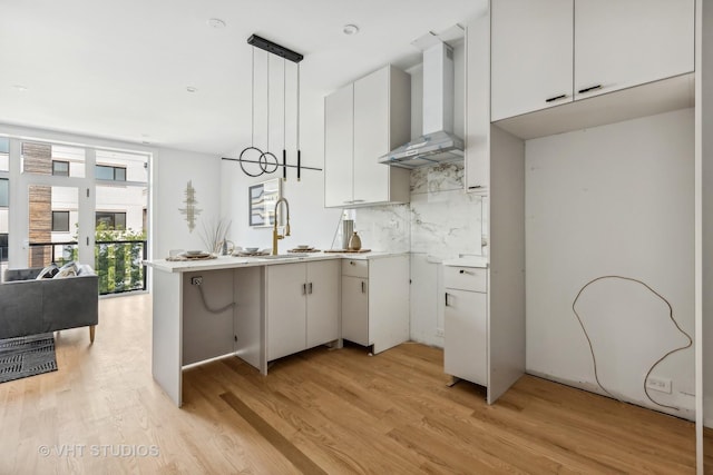 kitchen featuring backsplash, decorative light fixtures, white cabinetry, and wall chimney exhaust hood