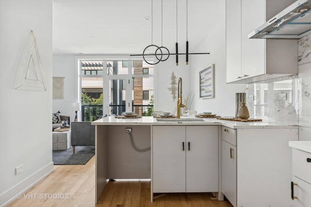 kitchen with sink, wall chimney range hood, an inviting chandelier, white cabinets, and light wood-type flooring