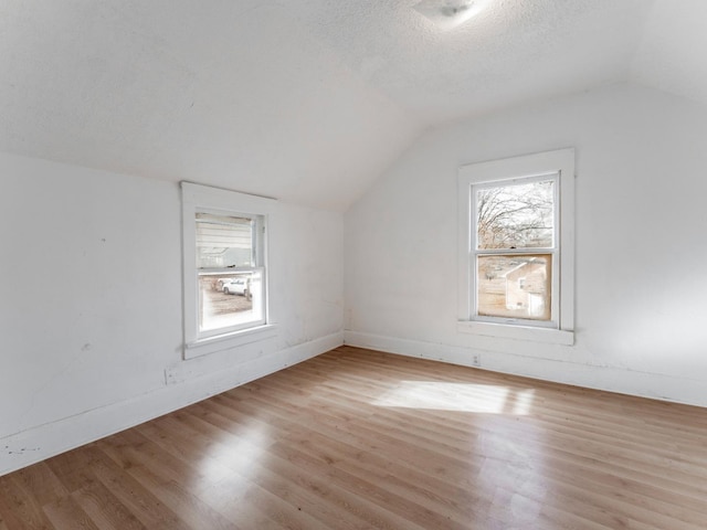 additional living space with a textured ceiling, light wood-type flooring, and vaulted ceiling