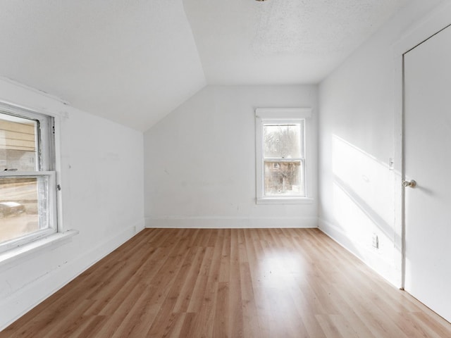 additional living space featuring a textured ceiling, light hardwood / wood-style flooring, and lofted ceiling