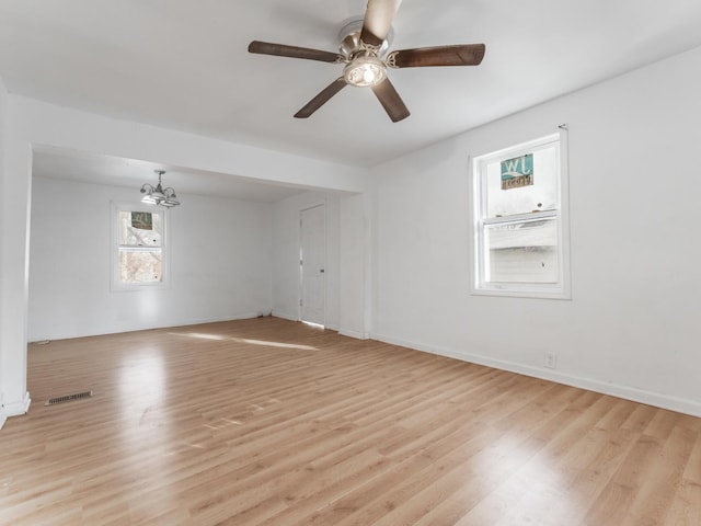 unfurnished room with ceiling fan with notable chandelier and light hardwood / wood-style floors