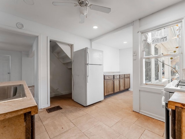 kitchen featuring stove, white refrigerator, sink, ceiling fan, and light tile patterned flooring