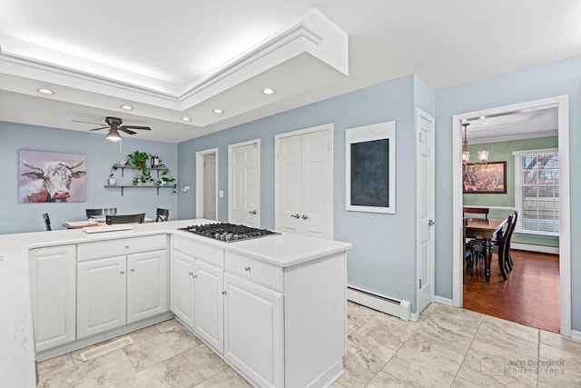 kitchen featuring white cabinetry, baseboard heating, kitchen peninsula, stainless steel gas stovetop, and ceiling fan with notable chandelier