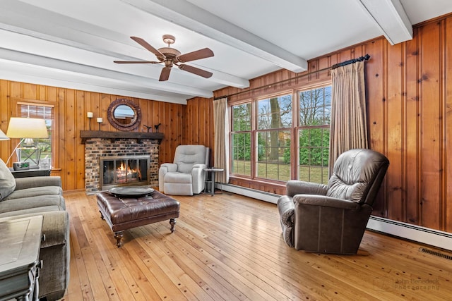 living room with hardwood / wood-style floors, a baseboard heating unit, a brick fireplace, ceiling fan, and beam ceiling