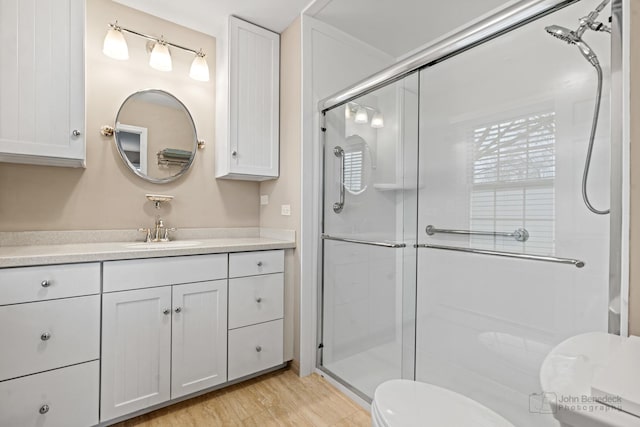 bathroom featuring wood-type flooring, vanity, toilet, and a shower with shower door