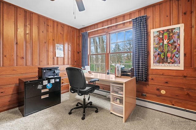 carpeted home office with baseboard heating, ceiling fan, and wooden walls