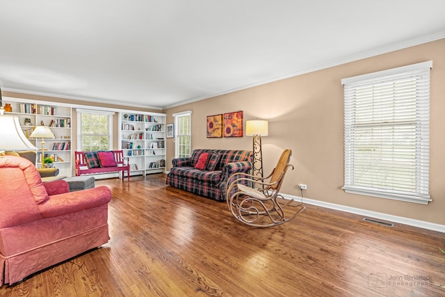 living room featuring hardwood / wood-style floors, built in features, baseboard heating, and ornamental molding