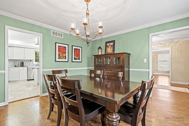 dining area featuring crown molding, light parquet flooring, and an inviting chandelier