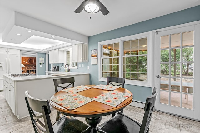 dining space with ceiling fan, sink, a baseboard radiator, and a tray ceiling