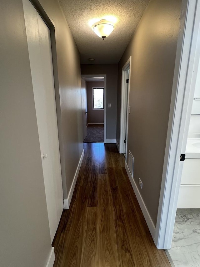 hallway with a textured ceiling and dark hardwood / wood-style floors