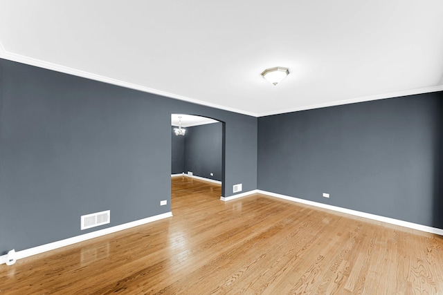 spare room with hardwood / wood-style flooring, ornamental molding, and an inviting chandelier