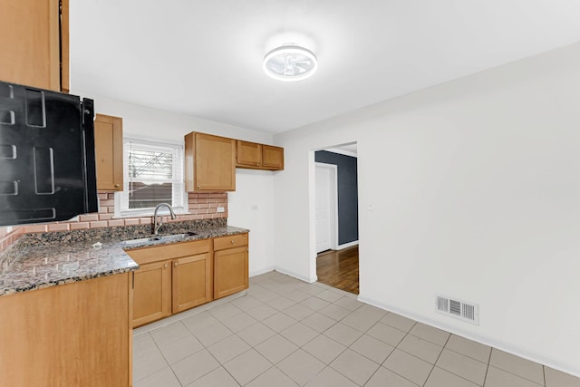 kitchen featuring tasteful backsplash, dark stone counters, and sink