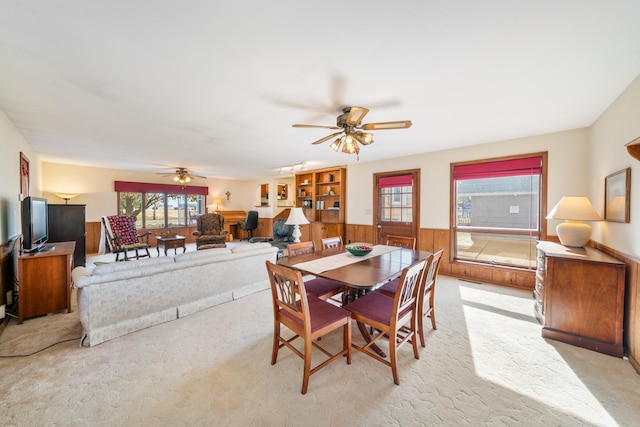 carpeted dining space with wood walls and ceiling fan