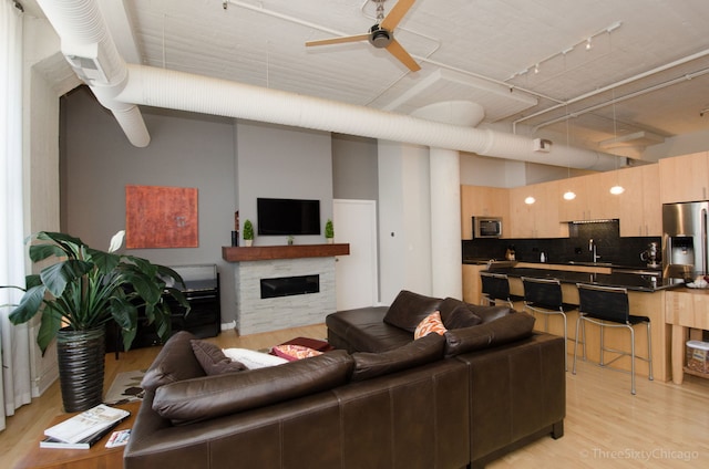 living room featuring ceiling fan, sink, a stone fireplace, track lighting, and light wood-type flooring