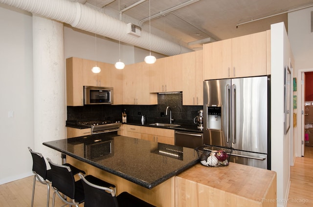 kitchen featuring decorative light fixtures, light brown cabinetry, stainless steel appliances, and dark stone counters