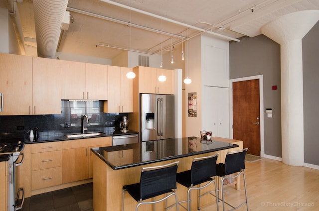 kitchen featuring appliances with stainless steel finishes, sink, light brown cabinets, a high ceiling, and a kitchen island