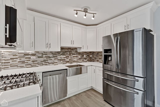 kitchen with backsplash, white cabinets, sink, light wood-type flooring, and appliances with stainless steel finishes