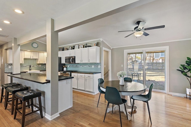 kitchen with a breakfast bar area, light hardwood / wood-style flooring, ornamental molding, stainless steel appliances, and white cabinets