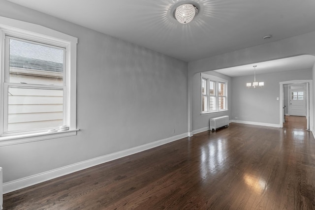 spare room with dark hardwood / wood-style floors, radiator, and an inviting chandelier