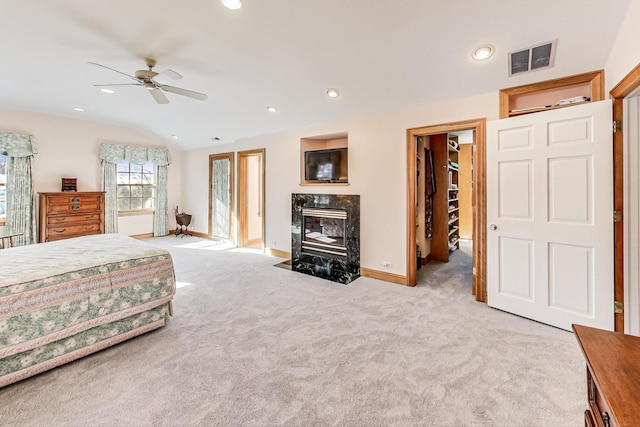 bedroom with vaulted ceiling, light colored carpet, ceiling fan, a fireplace, and a walk in closet