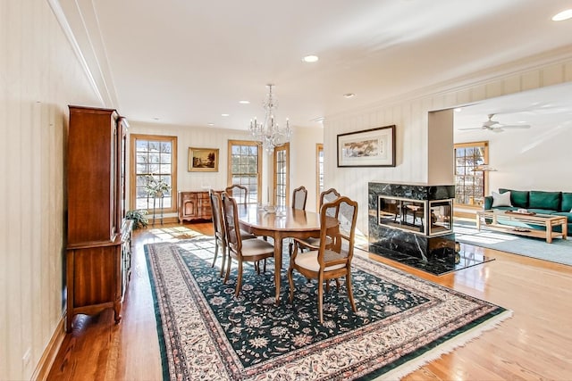 dining area with ceiling fan with notable chandelier, wood-type flooring, a premium fireplace, and ornamental molding