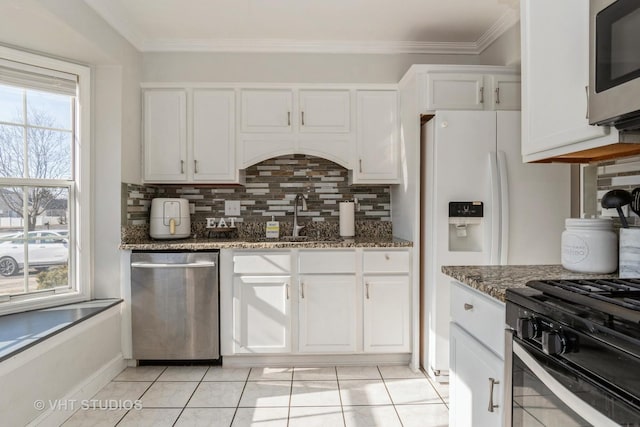 kitchen with appliances with stainless steel finishes, tasteful backsplash, light tile patterned floors, white cabinets, and dark stone counters