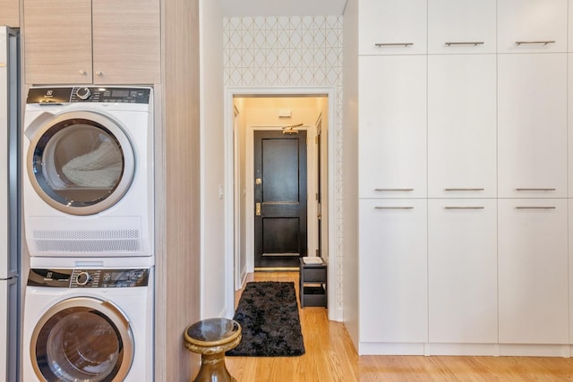 washroom with stacked washer and dryer, cabinets, and light hardwood / wood-style floors