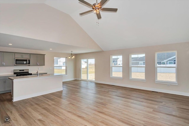 unfurnished living room featuring ceiling fan with notable chandelier, light hardwood / wood-style floors, high vaulted ceiling, and sink