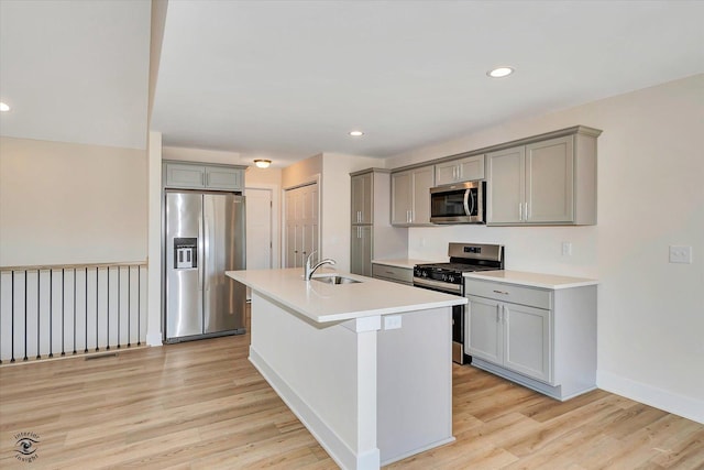 kitchen with sink, stainless steel appliances, an island with sink, light hardwood / wood-style floors, and gray cabinets