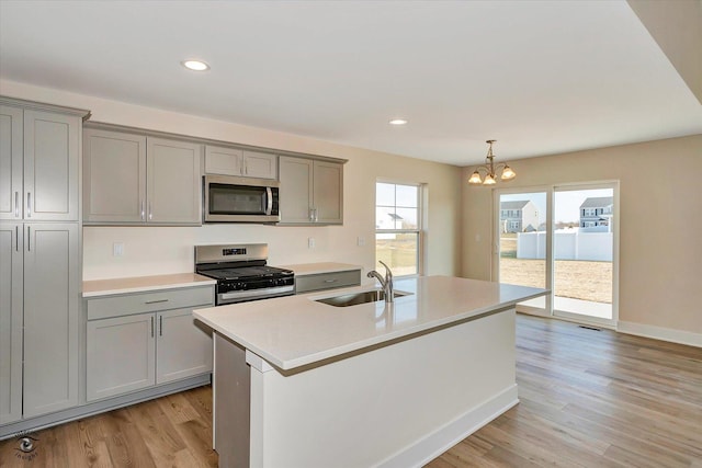 kitchen with gray cabinetry, stainless steel appliances, sink, a center island with sink, and a notable chandelier