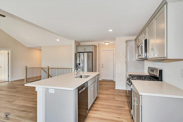 kitchen with gray cabinetry, sink, an island with sink, light hardwood / wood-style floors, and appliances with stainless steel finishes