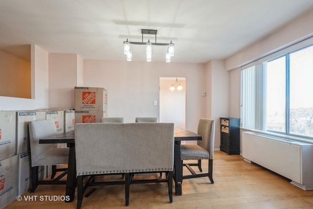 dining area featuring light wood-type flooring, radiator, and a notable chandelier