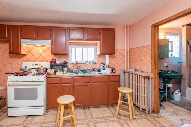 kitchen featuring radiator heating unit, sink, a textured ceiling, light tile patterned flooring, and white gas range oven