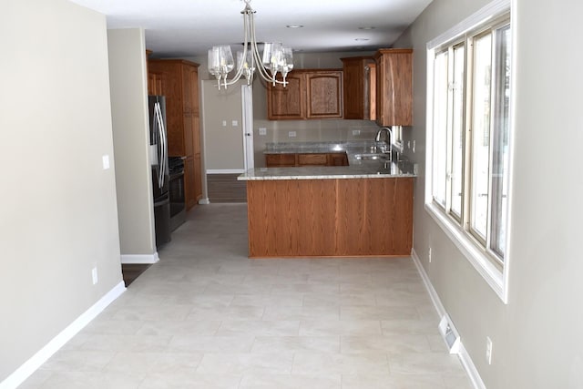 kitchen with kitchen peninsula, sink, decorative light fixtures, a chandelier, and stainless steel refrigerator