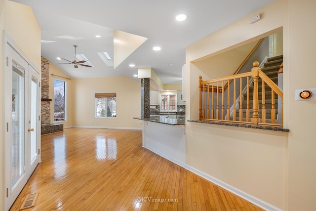 kitchen with ceiling fan, kitchen peninsula, dark stone counters, light hardwood / wood-style floors, and vaulted ceiling