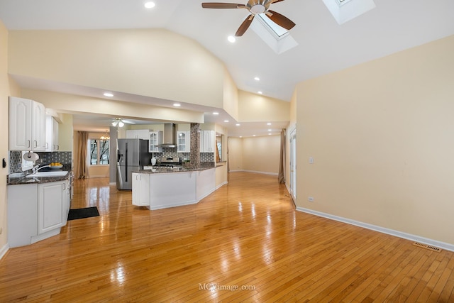 kitchen featuring high vaulted ceiling, white cabinets, a skylight, light wood-type flooring, and appliances with stainless steel finishes