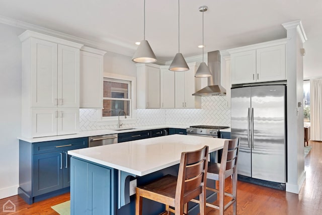 kitchen featuring a kitchen island, white cabinets, stainless steel appliances, blue cabinetry, and wall chimney range hood