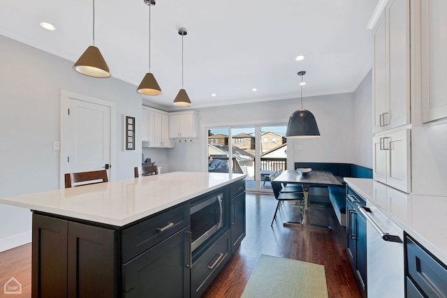 kitchen with dark wood-type flooring, hanging light fixtures, ornamental molding, a kitchen island, and white cabinets