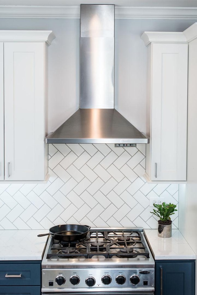 kitchen featuring gas range, blue cabinetry, wall chimney range hood, and ornamental molding