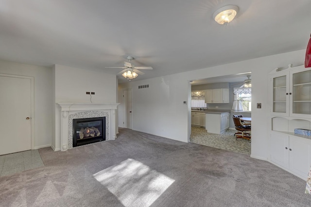 unfurnished living room with a fireplace, light colored carpet, and ceiling fan