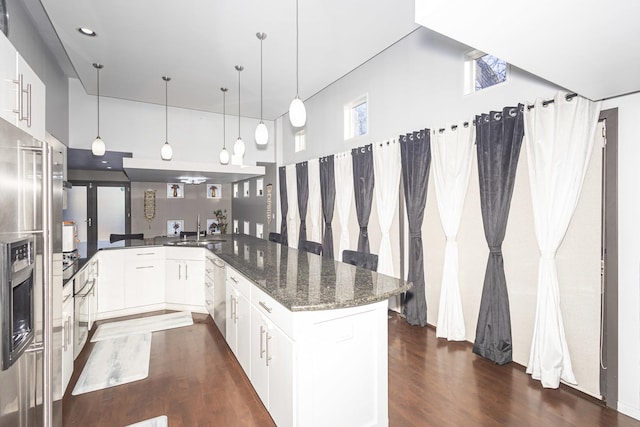 kitchen with decorative light fixtures, dark stone countertops, kitchen peninsula, sink, and white cabinetry